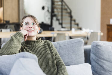 Thoughtful woman sitting on sofa in living room at home - MCVF00786