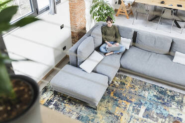 Young woman using laptop while sitting on sofa in living room at home - MCVF00787