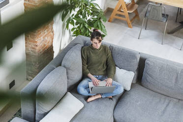 Woman using laptop on sofa at home - MCVF00788