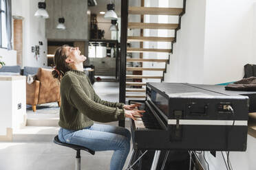 Cheerful woman playing piano at home - MCVF00792