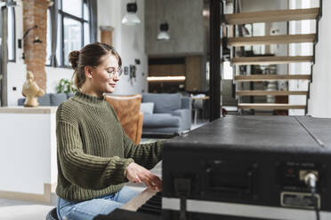 Woman wearing sweater playing piano in modern home - MCVF00794