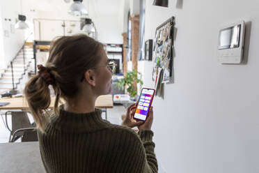 Junge Frau nutzt die Smart-Home-Funktion ihres Mobiltelefons zu Hause - MCVF00796