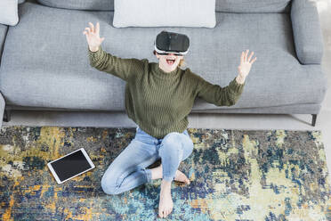 Fröhliche Frau gestikuliert bei der Verwendung eines Virtual-Reality-Headsets zu Hause - MCVF00799