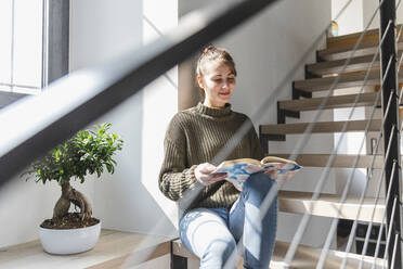 Image of A young woman sitting on a staircase reads a book