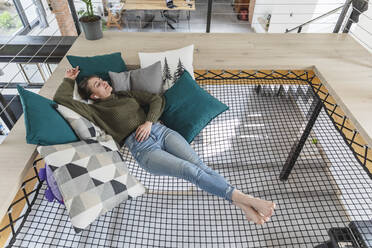 Relaxed young woman lying on hammock in modern home stock photo