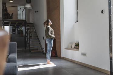 Sonnenlicht fällt auf eine Frau, die zu Hause im Wohnzimmer steht - MCVF00825