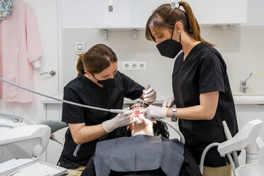 Zahnärztinnen reinigen die Zähne eines Patienten in einer medizinischen Klinik - DLTSF01875