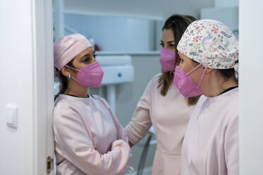 Female dentists wearing protective face masks discussing at doorway in clinic - DLTSF01879