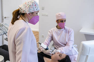 Zahnärztinnen im mittleren Erwachsenenalter bei der Untersuchung der Zähne einer Frau in einer Klinik - DLTSF01883