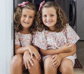Lächelnde süße Schwestern, die zusammen an der Tür sitzen - JRVF00536