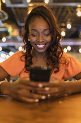Lächelnde Frau mit Smartphone in einer Bar - JRVF00544