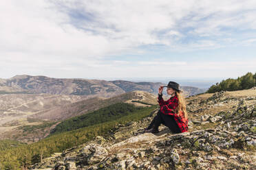 Junge Frau mit Hut, die in den Ferien auf einem Berg sitzt und nachdenkt - RSGF00665