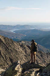 Man with backpack looking at mountain while standing on rock during vacations - RSGF00670