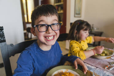 Boy smiling by sister while having food at home - MGIF01104