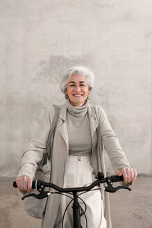 Glückliche Frau im Trenchcoat auf dem Fahrrad - ASSF00003