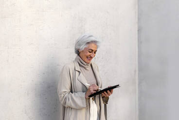 Glückliche Frau mit digitalem Tablet vor einer Wand - ASSF00019