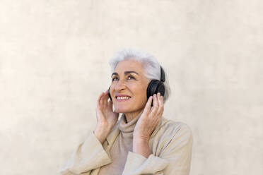 Lächelnde Frau, die mit Kopfhörern vor einer Wand träumt - ASSF00033