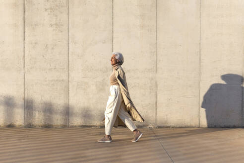 Ältere Frau im Trenchcoat geht auf dem Fußweg - ASSF00039