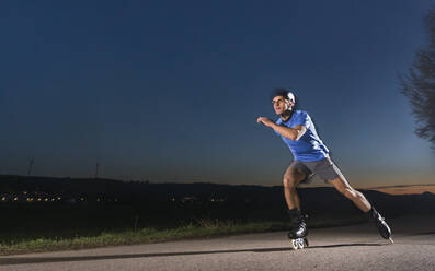 Young man with speed skating on road during dusk - STSF02939