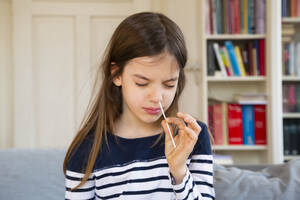 Girl with eyes closed putting cotton swab in nose while self testing at home - LVF09166