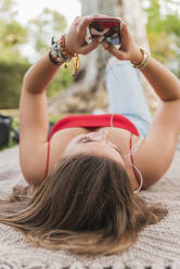 Young woman with mobile phone lying on back in park - JRVF00564