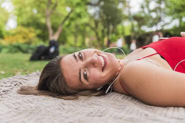 Happy young woman lying on blanket in park - JRVF00566