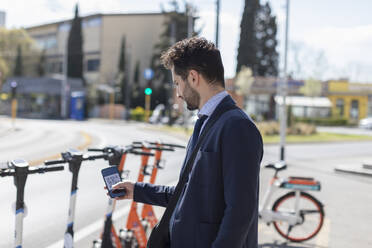Männlicher Unternehmer, der auf einem Parkplatz einen Elektroroller mit seinem Mobiltelefon aufschließt - EIF01004