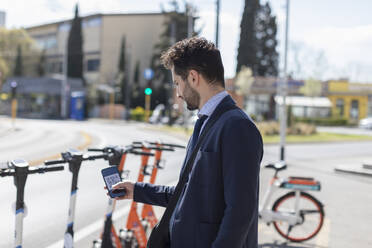 Male entrepreneur unlocking electric push scooter through mobile phone at parking lot - EIF01004