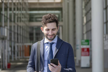 Lächelnder Unternehmer, der an einem sonnigen Tag ein Mobiltelefon benutzt - EIF01005