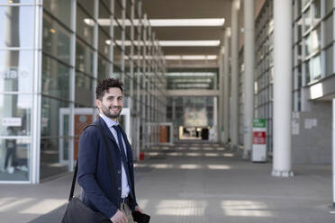 Smiling professional with shoulder bag on footpath - EIF01011