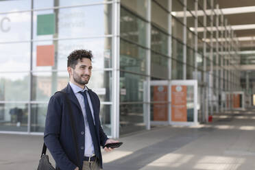 Businessman holding mobile phone while standing on footpath - EIF01012