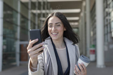 Lächelnde Geschäftsfrau mit Einwegbecher nimmt Selfie durch Smartphone - EIF01020