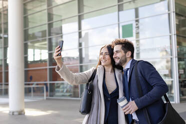 Lächelnde Unternehmerin, die ein Selfie mit einem Kollegen über ihr Handy macht - EIF01042