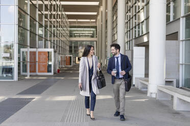 Male and female colleagues talking while walking on footpath - EIF01046