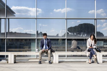Geschäftsleute sitzen auf einer Bank vor einem Gebäude - EIF01052