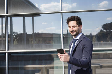 Männlicher Berufstätiger, der ein Mobiltelefon benutzt, während er vor einem Gebäude steht - EIF01055