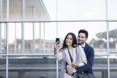 Professional couple taking selfie through mobile phone in front of building - EIF01058