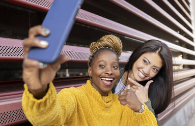 Fröhliche Freundinnen machen ein Selfie mit dem Smartphone an der Wand - JCCMF02233