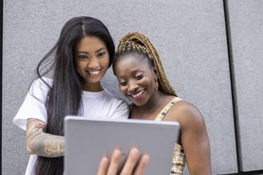 Freundinnen benutzen ein digitales Tablet an der Wand im Freien - JCCMF02248