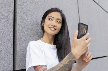 Hipster-Frau schaut weg und hält ihr Smartphone an die Wand - JCCMF02258
