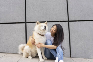 Mittlere erwachsene Frau sitzt mit Akita-Hund an der Wand - JCCMF02261