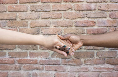 Female friends holding hands by brick wall - JCCMF02269