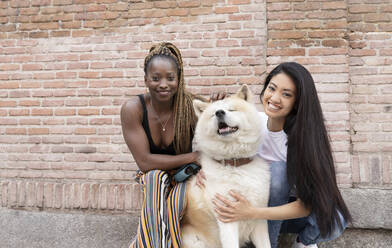 Multi-ethnic female friends with Akita Dog by brick wall - JCCMF02283