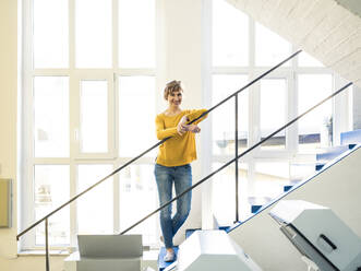 Smiling businesswoman leaning on railing in printing factory - JOSEF04211