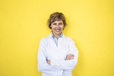 Smiling female scientist standing with arms crossed in front of wall - JOSEF04221