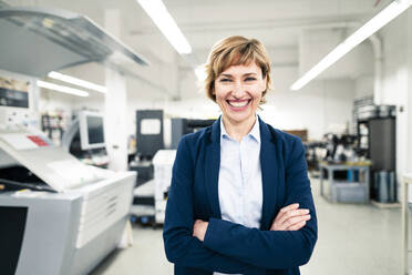 Cheerful businesswoman with arms crossed in printing factory - JOSEF04247