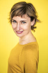 Mature woman staring while smiling by yellow background - JOSEF04262