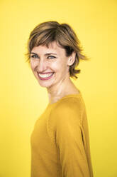 Cheerful mature woman standing by yellow background - JOSEF04263