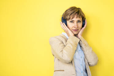 Unternehmerin mit Kopfhörern vor einer gelben Wand - JOSEF04290