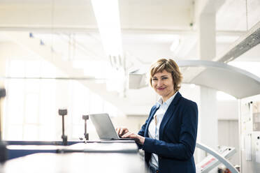 Lächelnde Geschäftsfrau vor einem Laptop in einer Druckwerkstatt - JOSEF04320